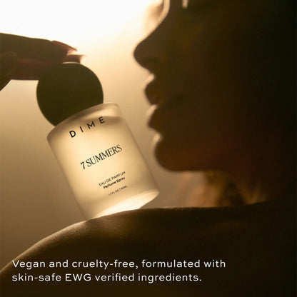 Clear glass perfume bottle labeled "7 Summers" held against a person's face in warm lighting.