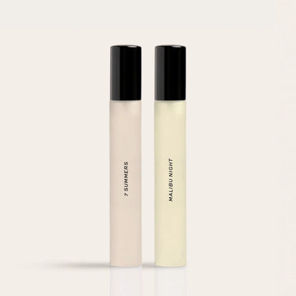 Two tall perfume rollerballs with black caps labeled "7 Summers" and "Malibu Night" in cream and pale yellow liquids.