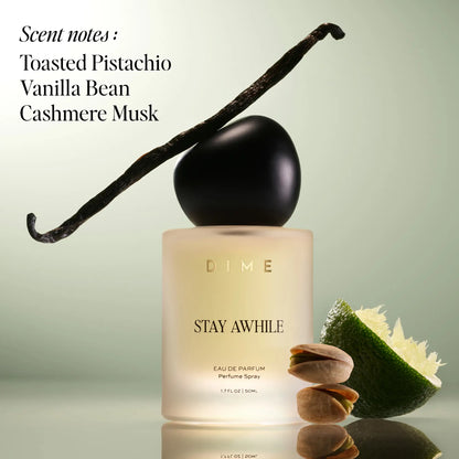 Cream-colored perfume bottle with black spherical cap and vanilla bean, topped with black curved stick, surrounded by pistach
