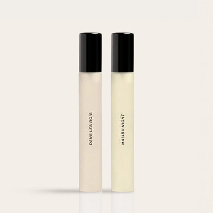 Two cylindrical fragrance bottles with black caps labeled "Daysles Bois" and "Malibu Night" in cream and pale yellow liquids.