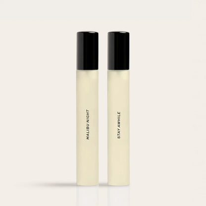 Two cylindrical fragrance bottles with black caps and cream-colored liquid, labeled "Malibu Night" and "Stay Awhile".