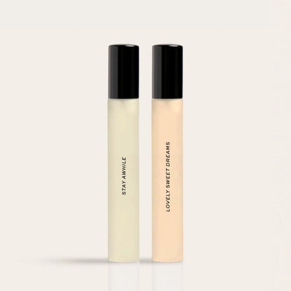 Two slim fragrance bottles with black caps labeled "Stay Awhile" and "Lovely Sweet Dreams" in pale yellow and peach liquids.