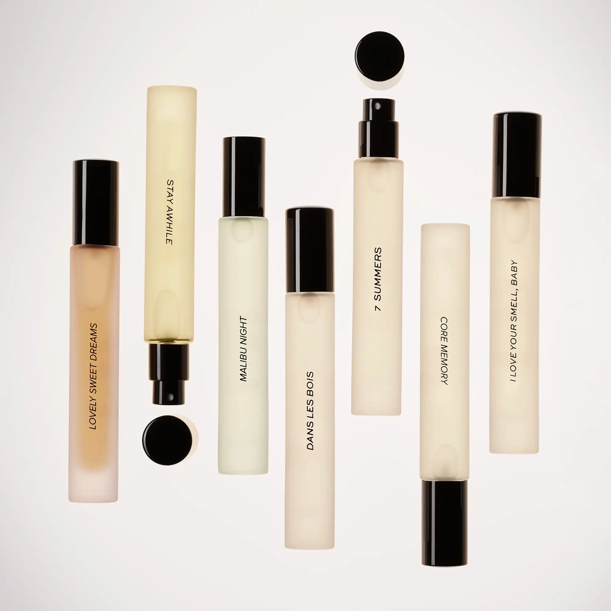 Small cylindrical perfume bottles with black caps in cream and pale gold liquid, arranged in rows against white background.
