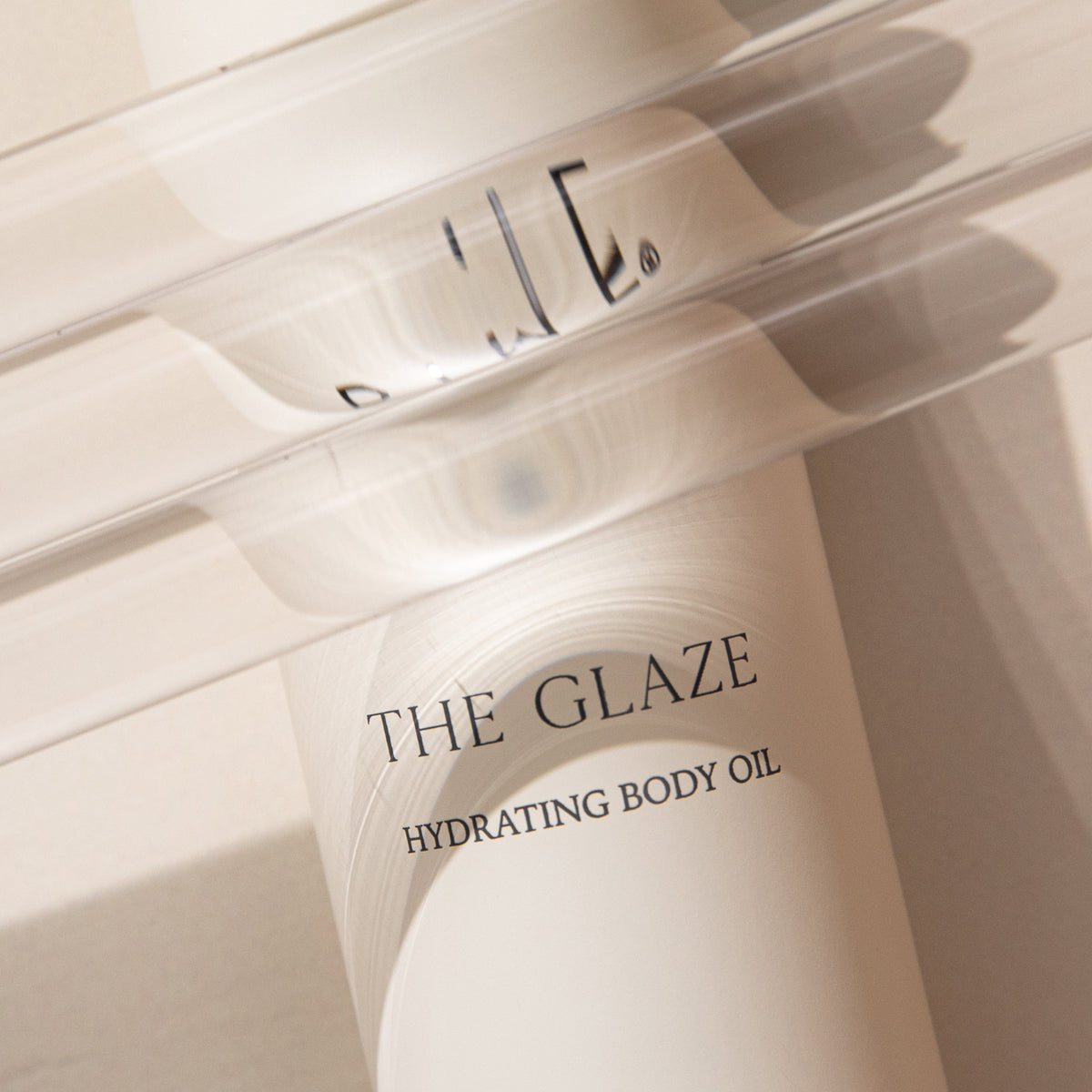 The Glaze hydrating body oil in a frosted glass bottle with pump dispenser on a light surface.
